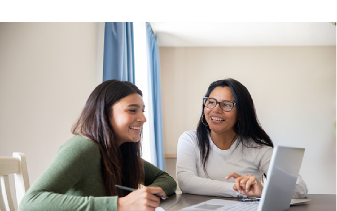 Two smiling women at a desk looking at a computer.