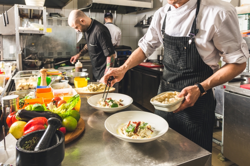 Two individuals preparing a meal in an industrial kitchen